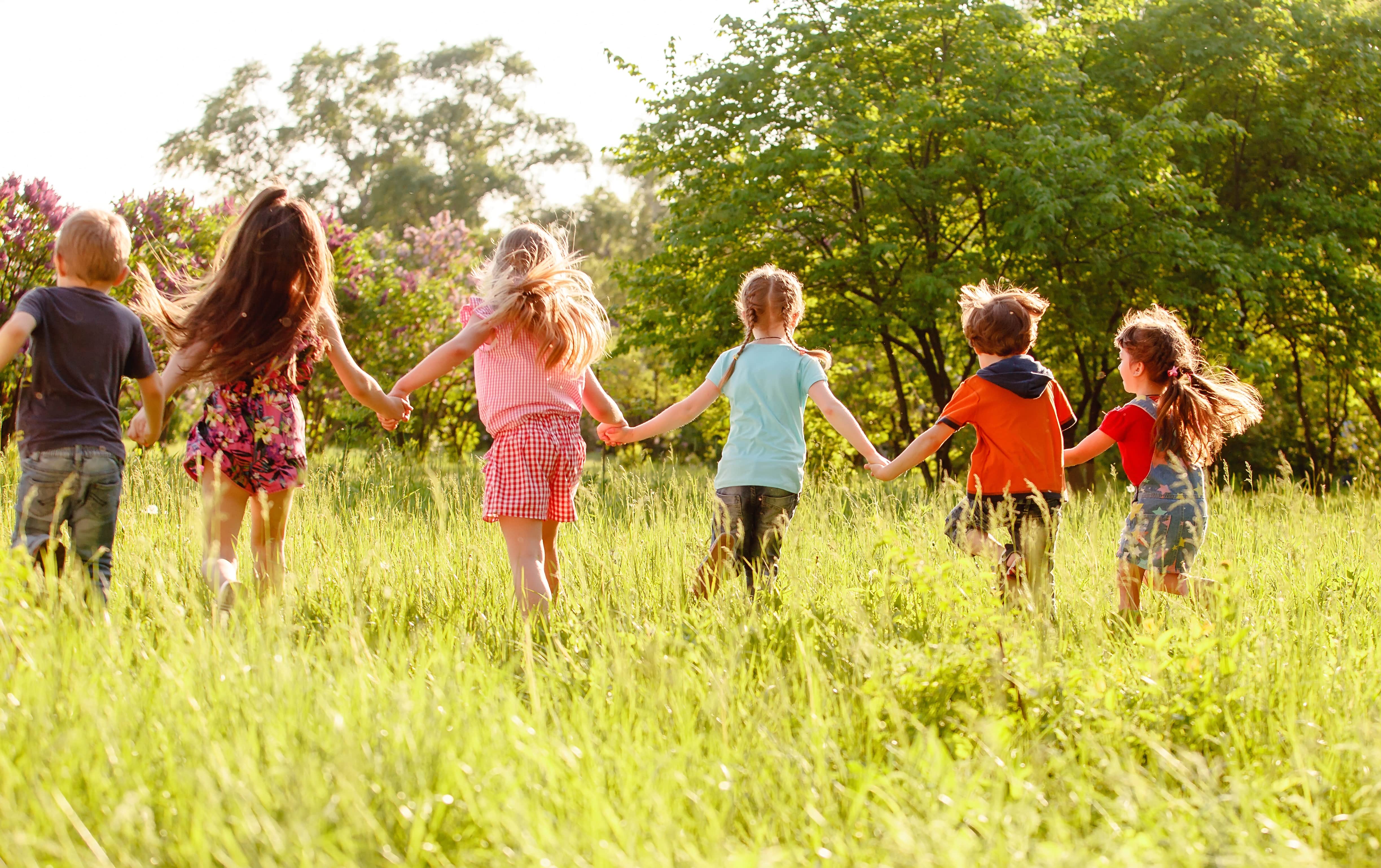 Sechs Kinder springen Hand in Hand über eine Wiese